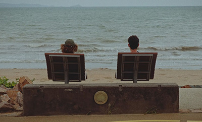 Two people sitting on the chairs at the beach overlooking the ocean.