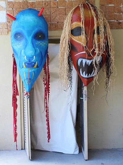 Two masks are hanging on 2 door frames set at an open angle.