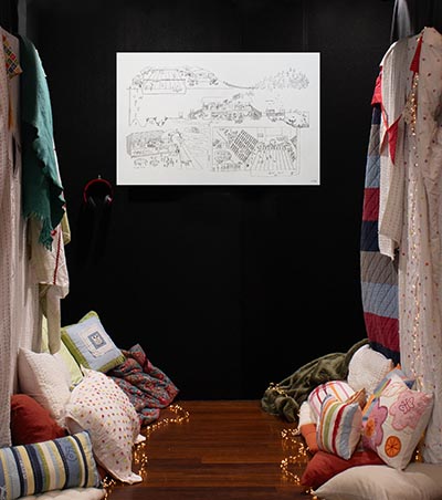 An installation features a space with pillows on both sides, a drawing hanging on a black wall, and a pair of headphones hanging off to the side. 