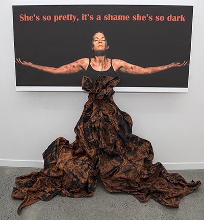 A woman standing in front of red text reading 'She's so pretty, it's a shame she's so dark' on a black background.