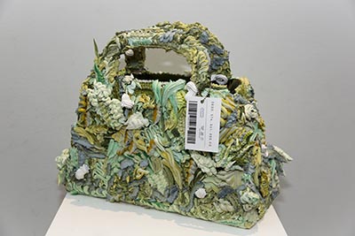 A sculpture is on display, featuring a handbag embellished with ornate decorations. Attached to the handbag is a price tag which reads $600,574,541,886.00.