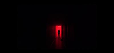 A silhouette of a person stands within a doorway bathed in red light, surrounded by darkness.