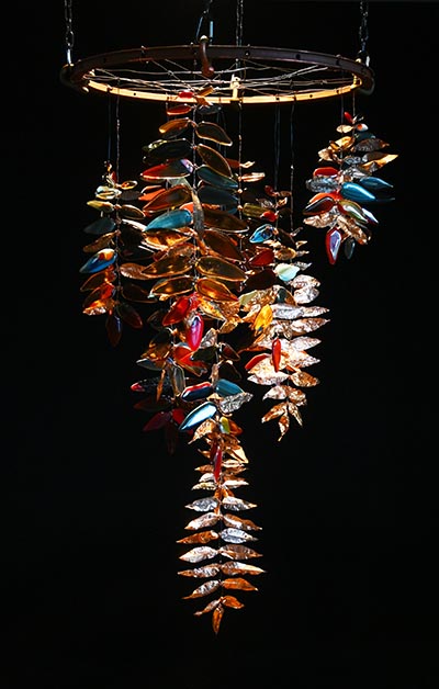 An installation showcasing leaf-shaped pieces crafted from metal and glass, suspended from a central structure at the top.