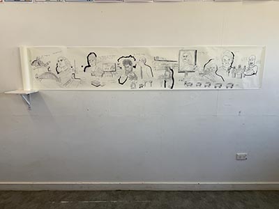 Drawing on paper displayed on the wall, extending to a roll of paper on a small shelf to the left.