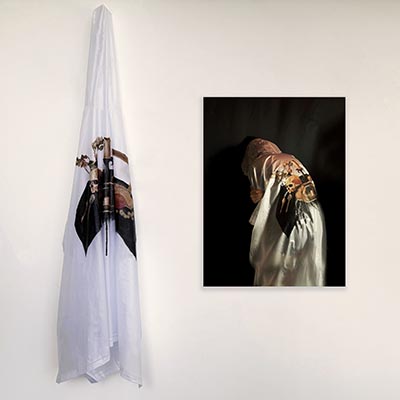Installation consisting of a white cloth with an illustration hanging on the left, and an image of a person wearing the cloth on the right, with the illustration visible on the back of the person