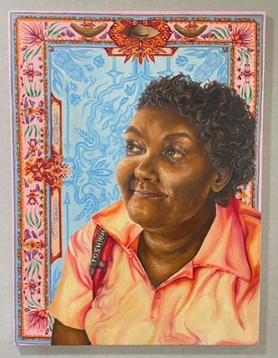 A portrait painting of an Indigenous woman named Carmen, positioned against a backdrop of woven carpet featuring objects of significance to her, interwoven with designs inspired by native flora.