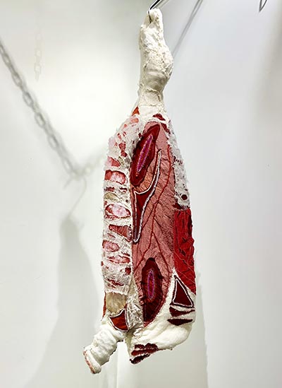 A sculpture featuring a hanging animal carcass crafted from textile materials.