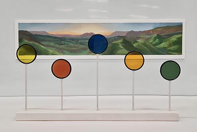 A landscape painting with a sculpture in front, featuring 5 transparent, coloured circular discs at varying heights, supported by pole-like structures and mounted on a base.