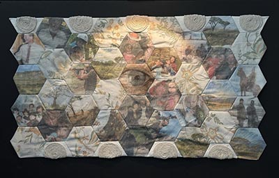 A quilt composed of repeated hexagon shapes featuring images and floral patterns. Some of the hexagons are adorned with thin ropes spiralled into circular forms.