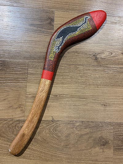 An image of a killer  boomerang featuring Indigenous art, including an emu painted in black.
