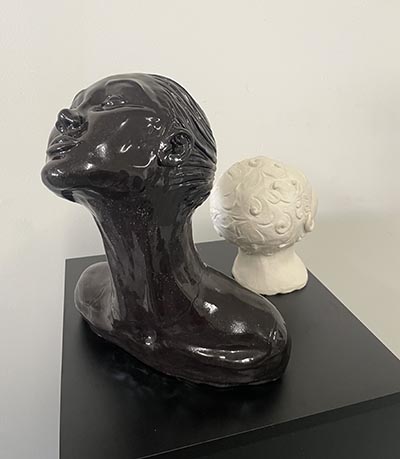 A sculpture of two human busts displayed on a plinth: one is a smaller, white child bust, while the larger black bust has a stretched neck and upward gaze.