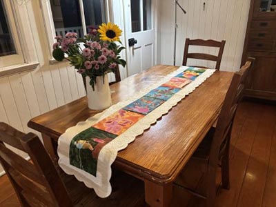 A realistic painting of a dining room showcasing a dining table adorned with a table runner and a vase filled with flowers.