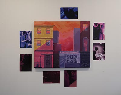 A large central painting of a cityscape featuring a laundromat, surrounded by seven smaller paintings on the wall. The smaller paintings depict close-up, clearer and more realistic scenes from the larger painting.