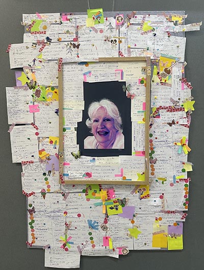 A drawn portrait is surrounded by collages of handwritten notes, with a wooden frame structure enclosing the portrait and incorporating some of the notes.