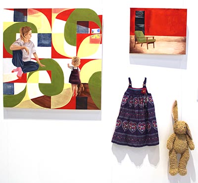 This artwork features 2 paintings, a child’s dress,and a rabbit plush toy, all hanging on the wall.